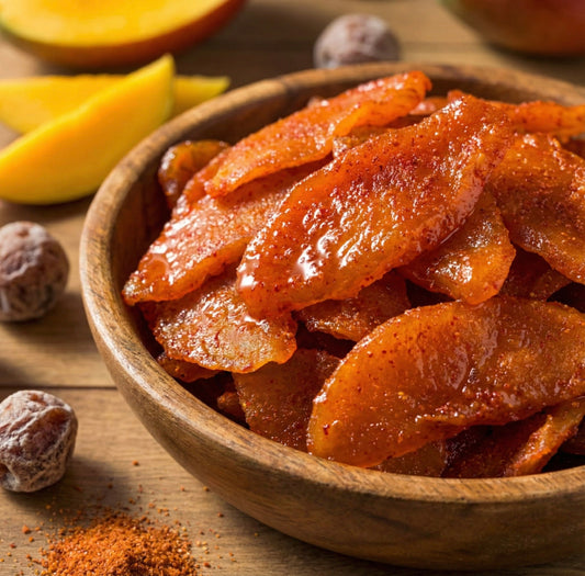 Wooden bowl filled with candied mango slices coated in sugar, surrounded by lemon wedges, nutmeg seeds, and spice powder on a rustic wooden surface